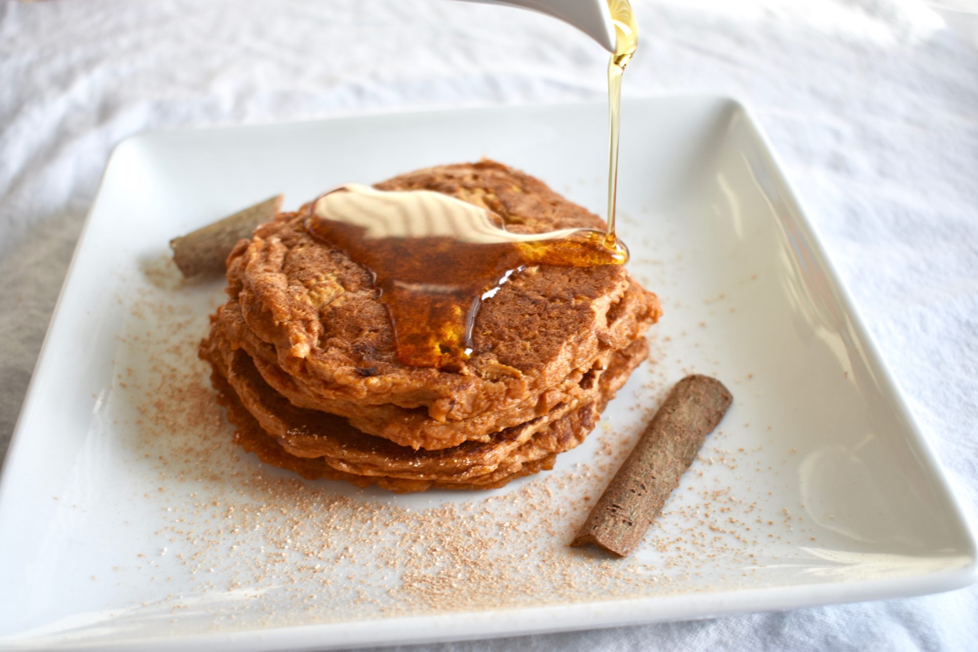 Syrup being poured over a stack of vegan cinnamon sweet potato pancakes